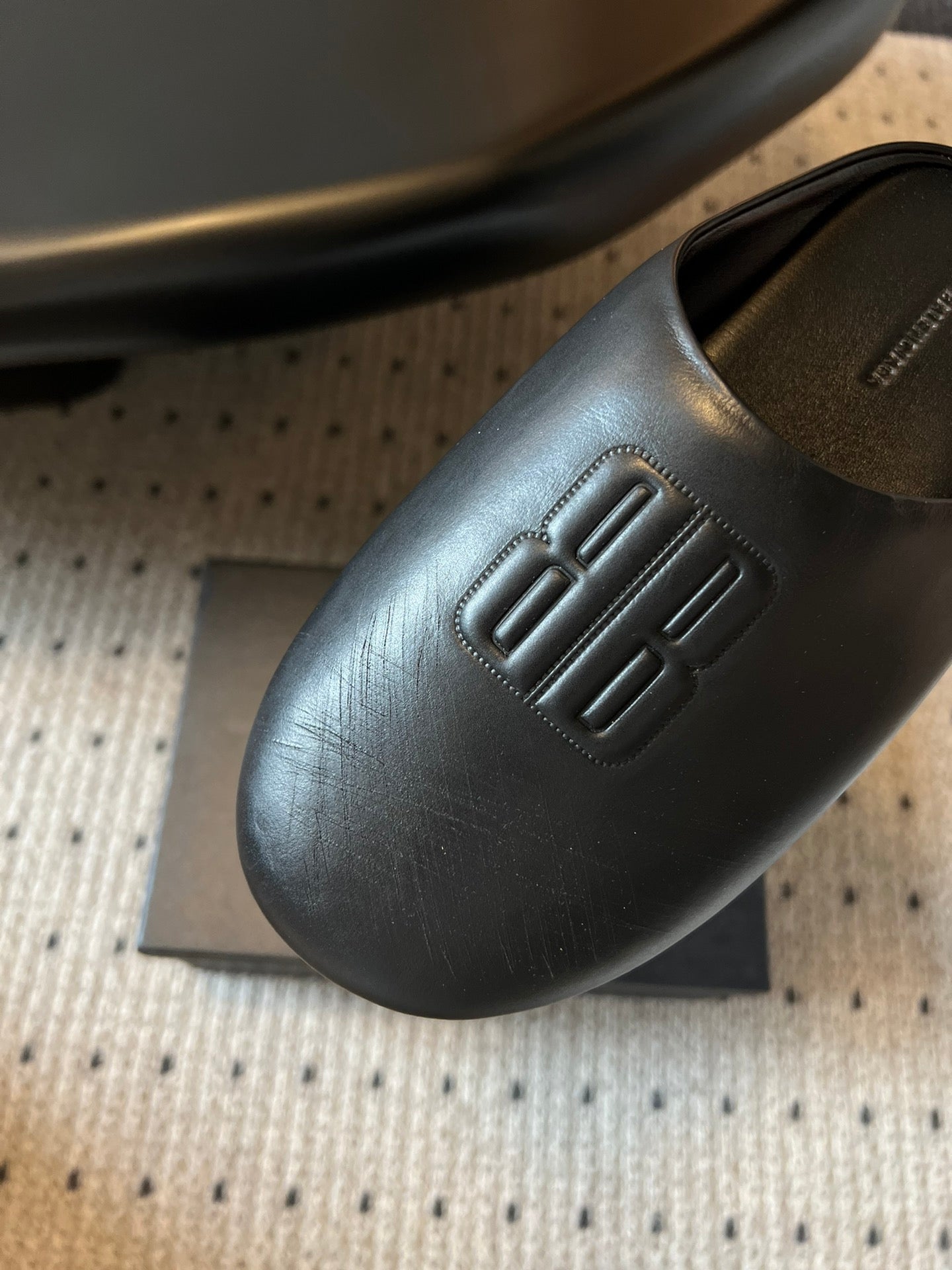 Balenciaga slide sandal close-up, embossed logo on dark leather upper