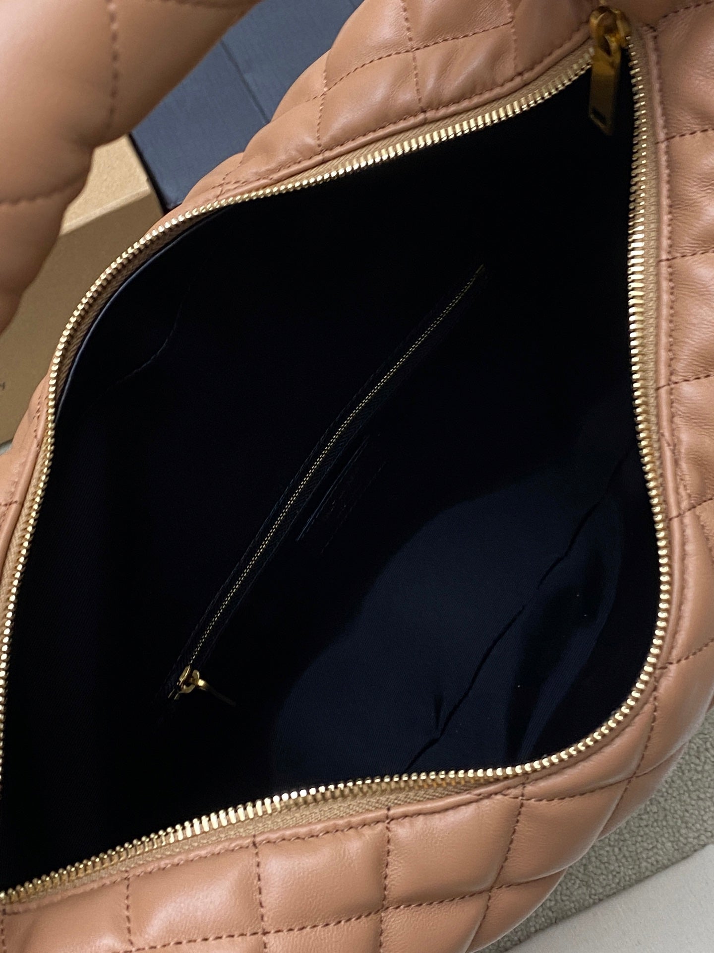 Open tan quilted hobo bag showing dark interior lining and gold zipper edge