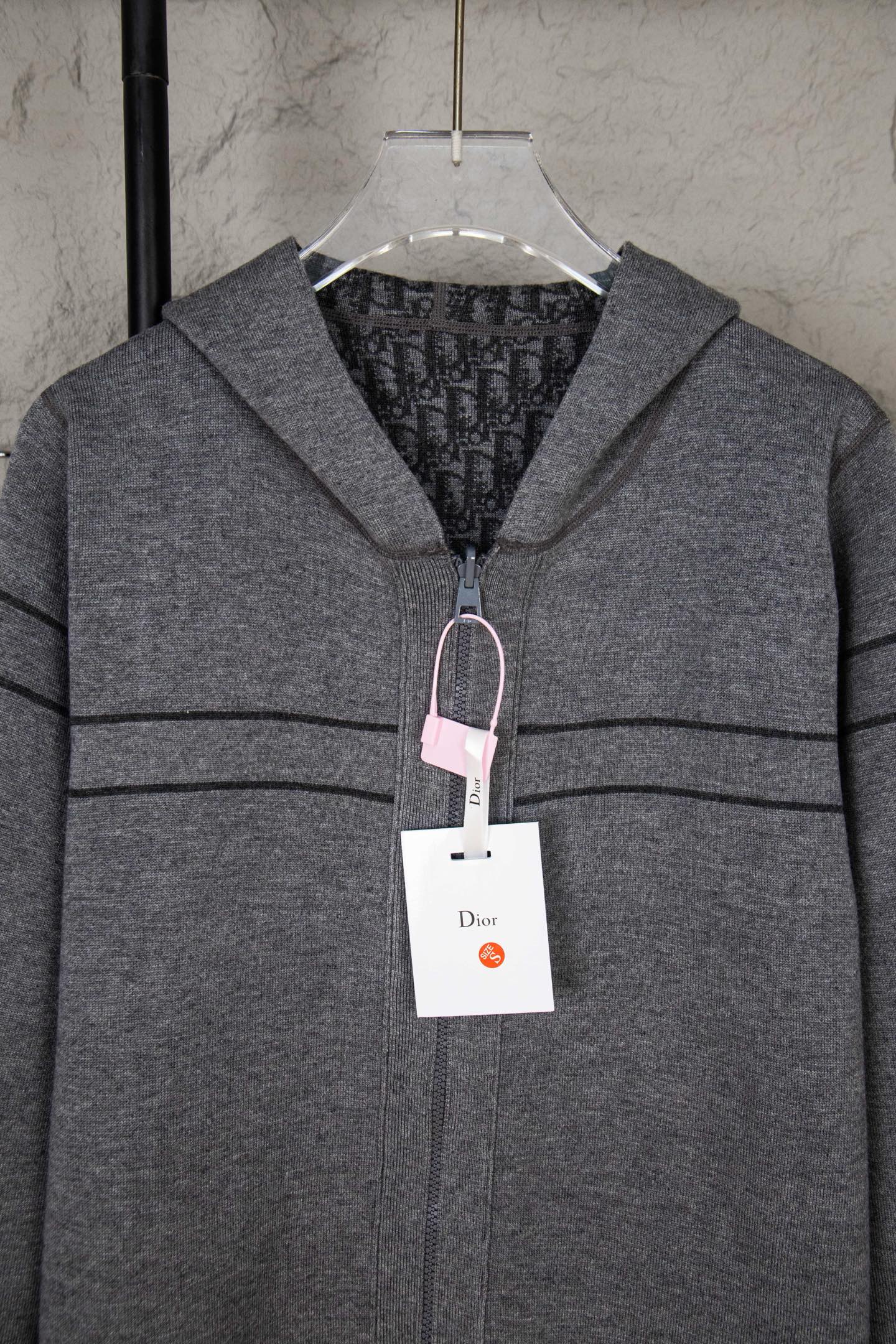 Gray Dior zip hoodie with hood, visible lining, and hanging garment tag