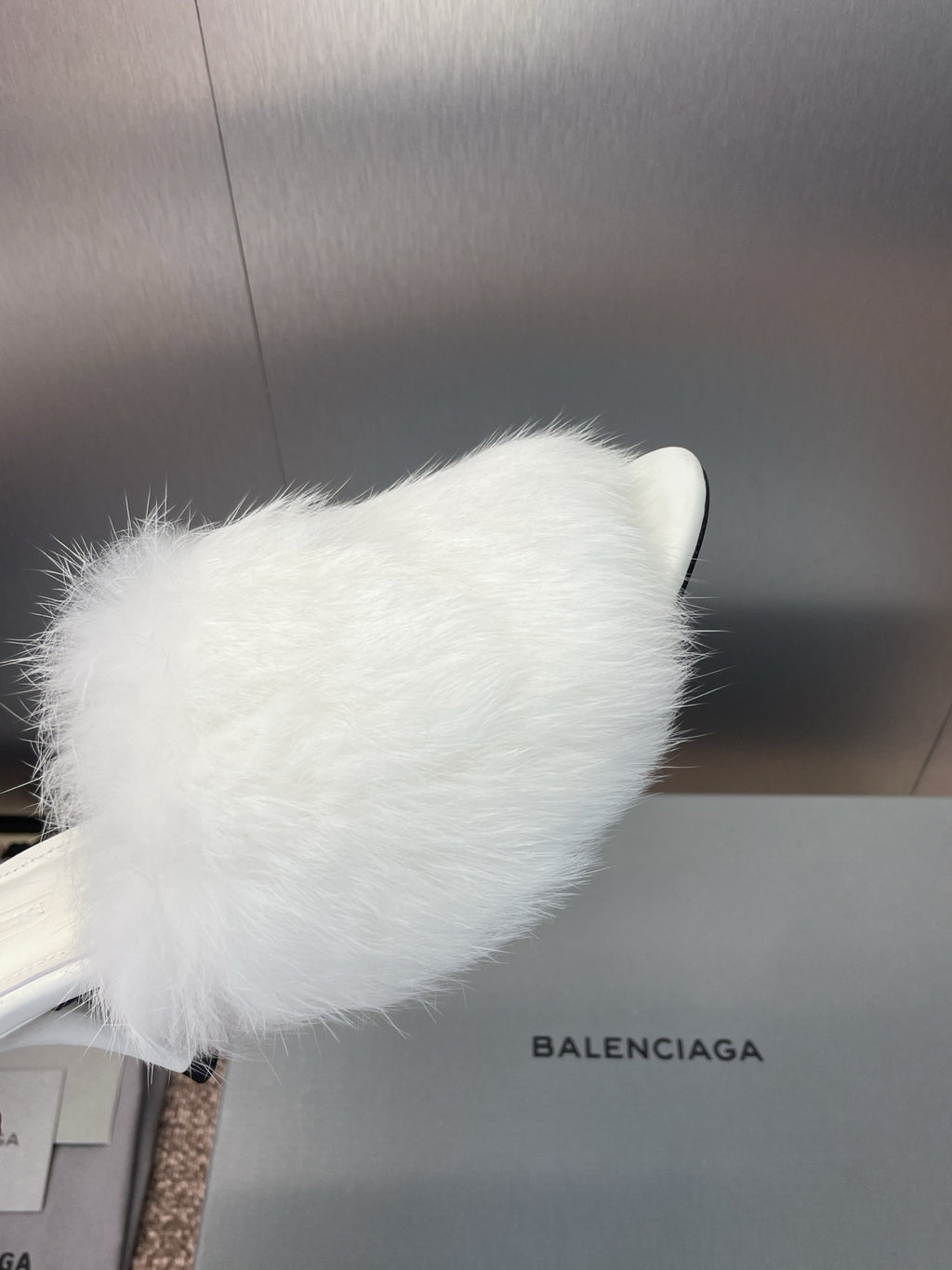 Close-up of white faux-fur slide sandal upper with slim stiletto heel.