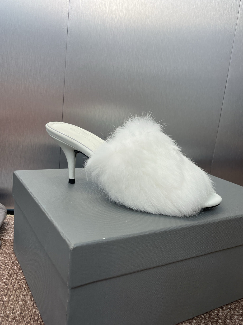 Single white faux-fur mule with slim stiletto heel on display box.