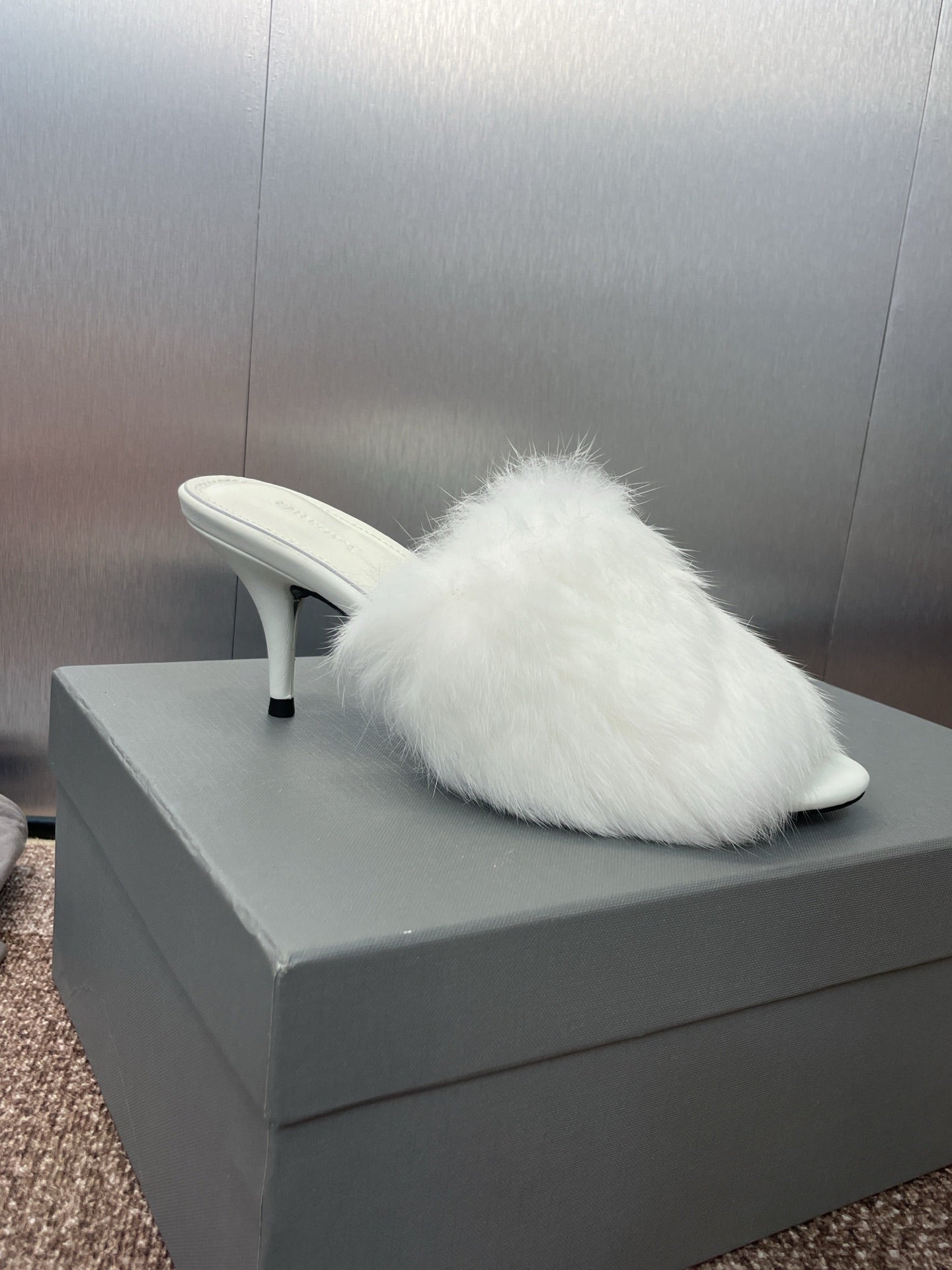 Single white faux-fur mule with slim stiletto heel on display box.