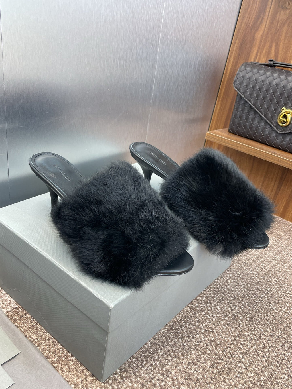 Black faux-fur slide sandals on a box, open toe with slender heels.