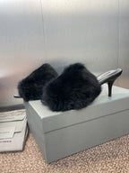 Black faux-fur slide sandals with open toe and slim high heel on box.