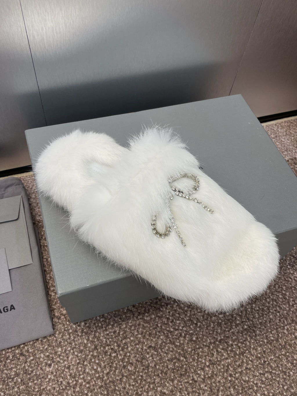 White faux-fur slide sandals with rhinestone bow detail on top, diagonal view