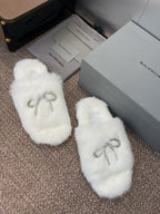 White fuzzy slide sandals with rhinestone bow detail on top, side view