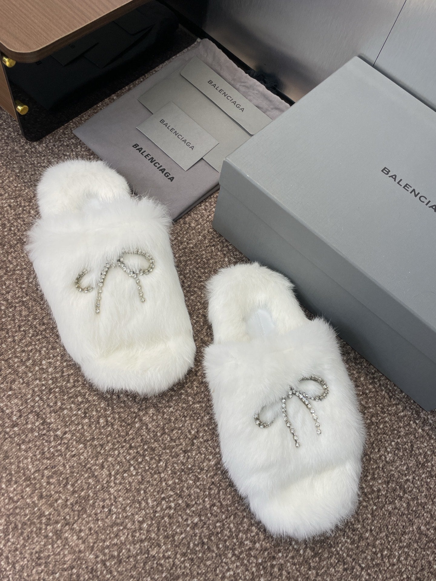 White fuzzy slide sandals with rhinestone bow detail on top, side view