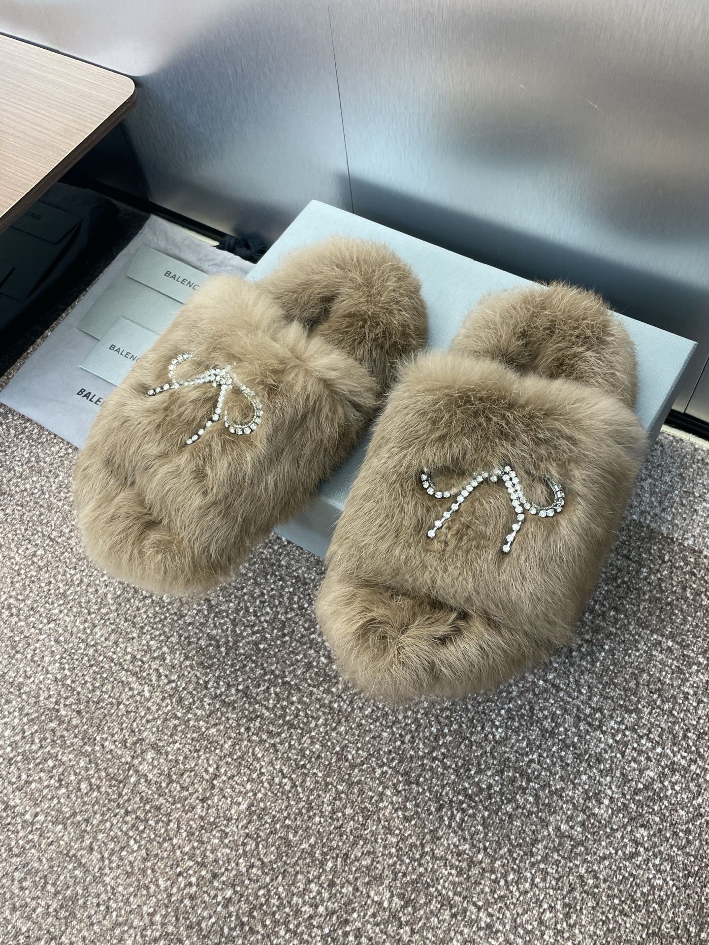 Taupe fuzzy slide sandals featuring a rhinestone bow on the strap