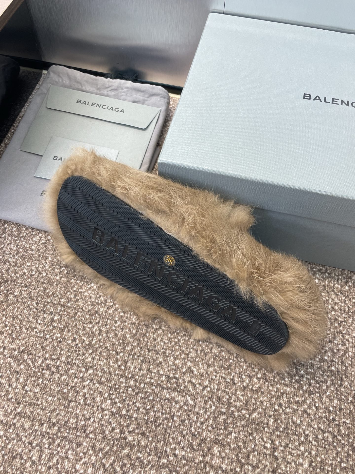 Tan fur slide sandal with dark rubber sole and stitched logo detail