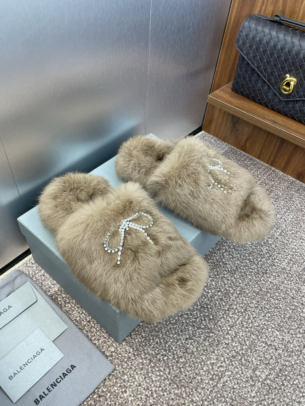 Fuzzy tan slide sandals with rhinestone bow detail across the front