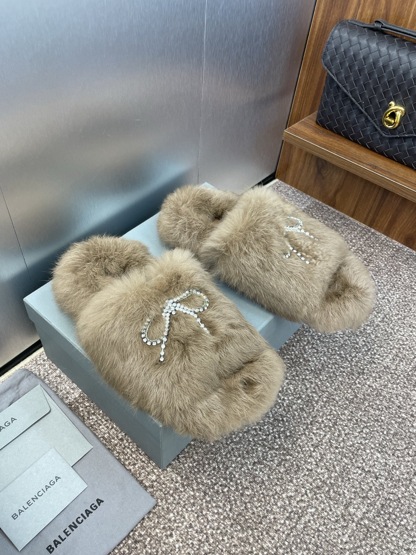 Fuzzy tan slide sandals with rhinestone bow detail across the front
