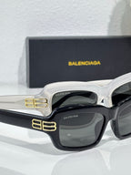 Balenciaga sunglasses closeup with white frames, dark lenses, gold logo detail on arm