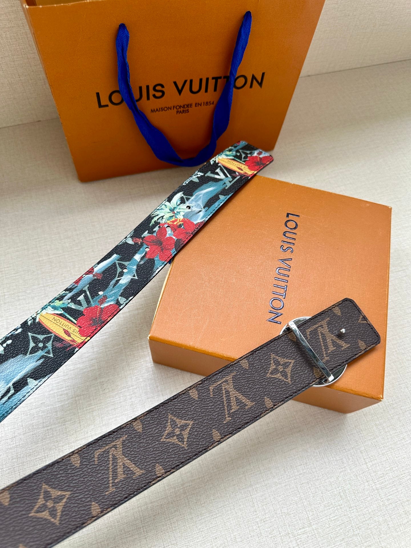 Louis Vuitton belt strap with multicolor floral print and gold-tone oval LV buckle, extended.
