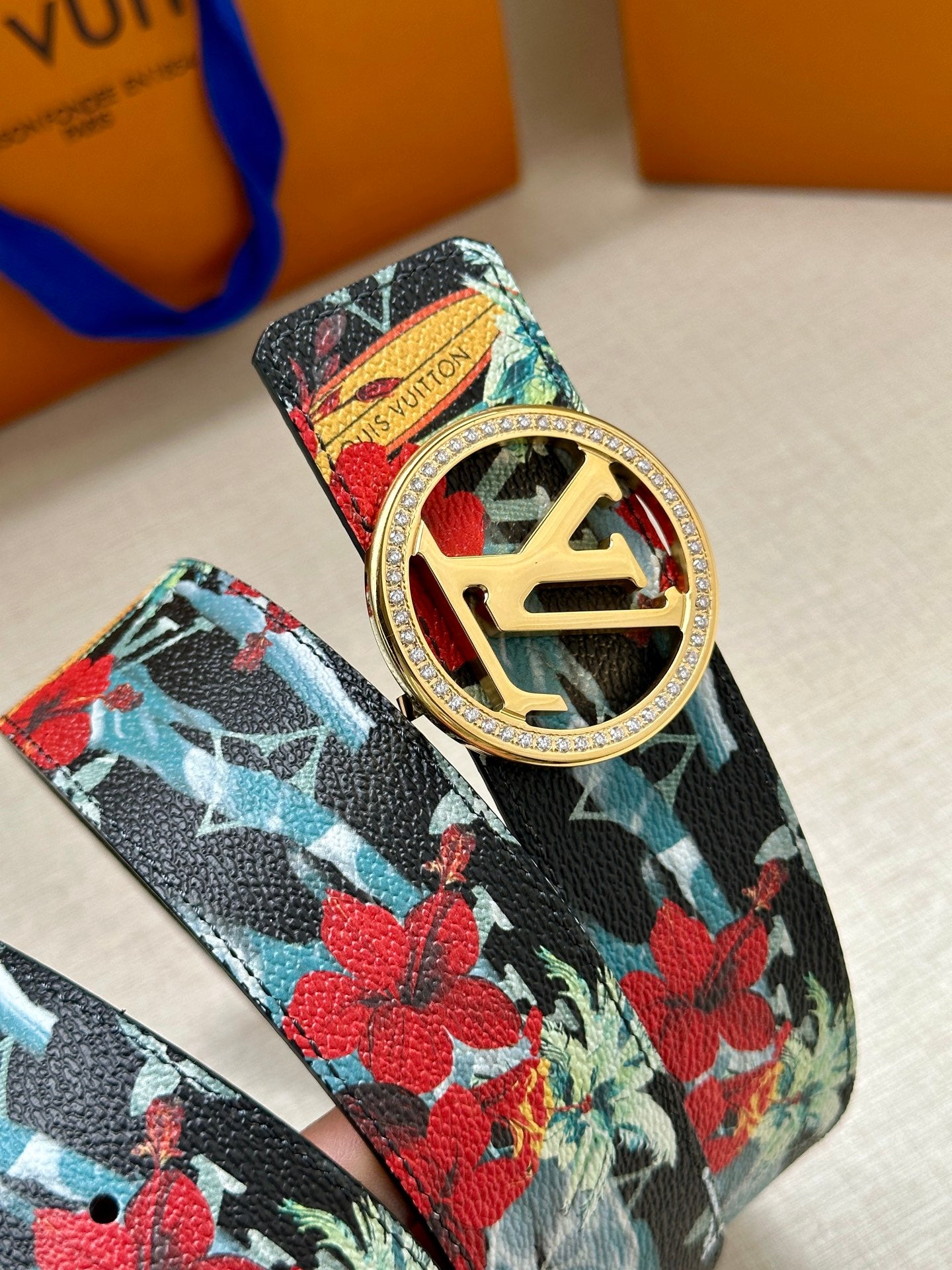 Louis Vuitton belt strap close-up with floral print and gold-tone oval LV buckle detail.