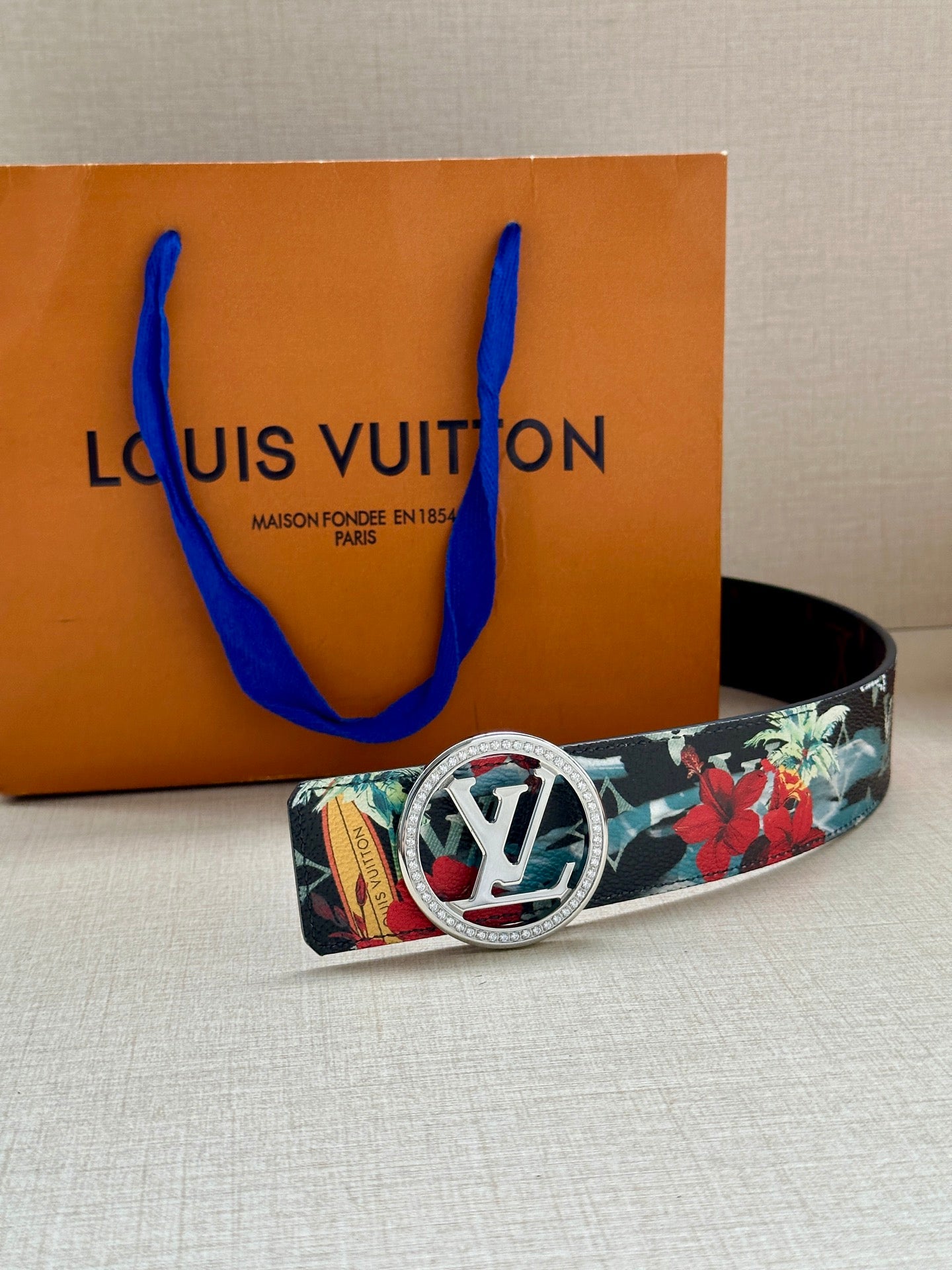 Louis Vuitton belt with floral strap and silver-tone oval LV buckle front, laid on white surface.