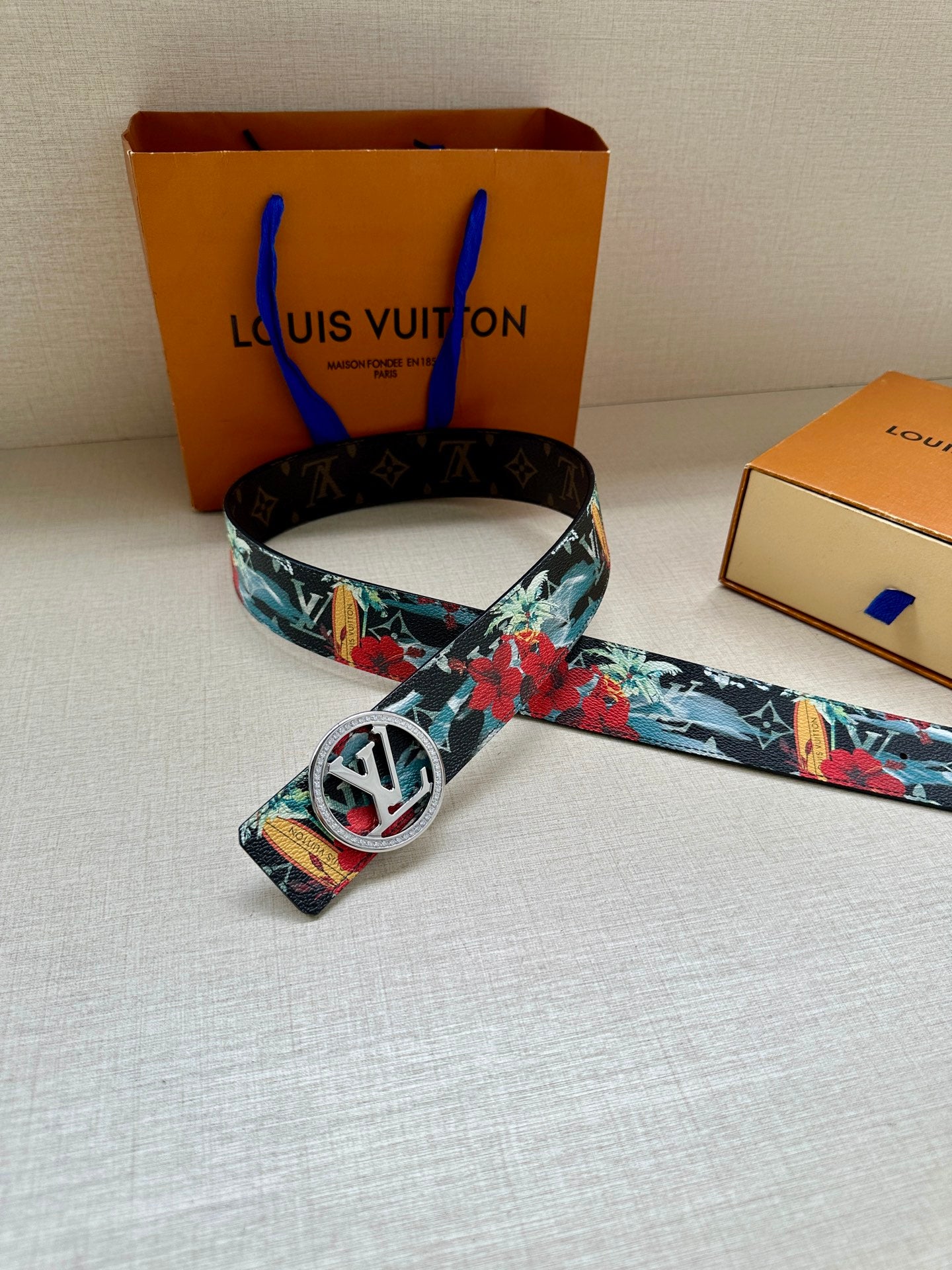 Louis Vuitton belt with floral-printed strap and gold-tone oval LV buckle, laid flat.