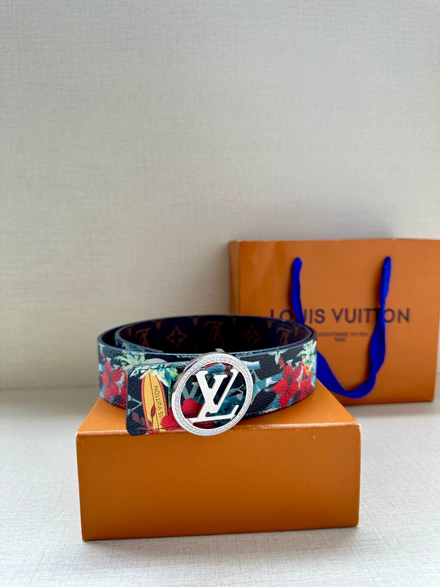 Louis Vuitton belt on display with floral strap and gold-tone oval LV buckle front.