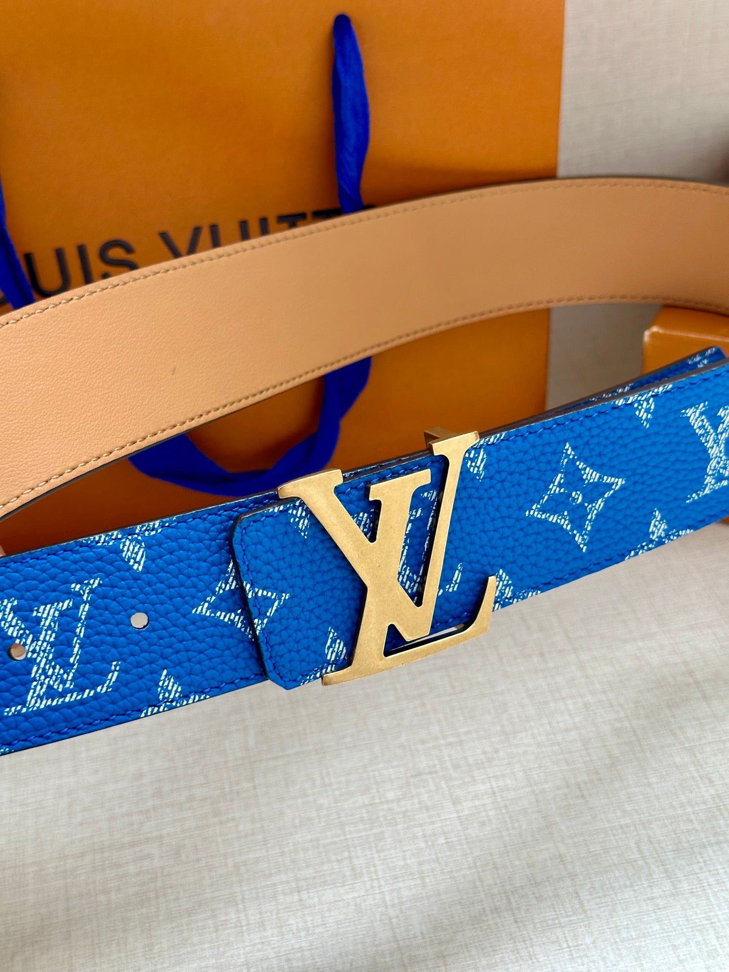 Blue monogram belt with tan leather strap and silver LV buckle close-up