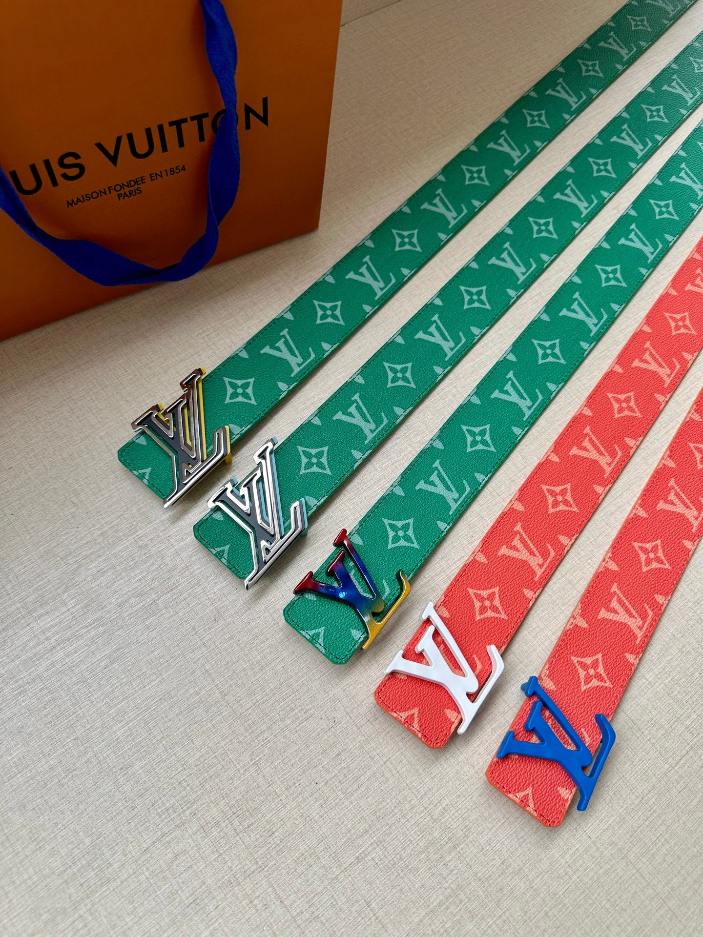 Green, red, and blue Louis Vuitton monogram belts with engraved LV buckles