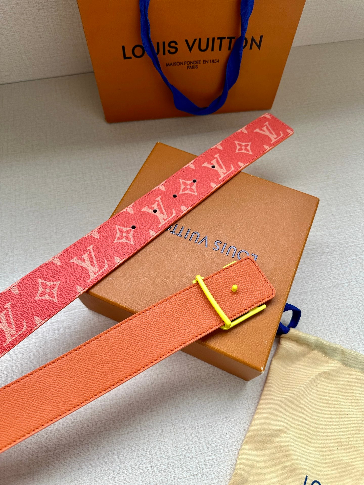 Louis Vuitton belt with red monogram strap and gold-tone LV buckle, laid on box.