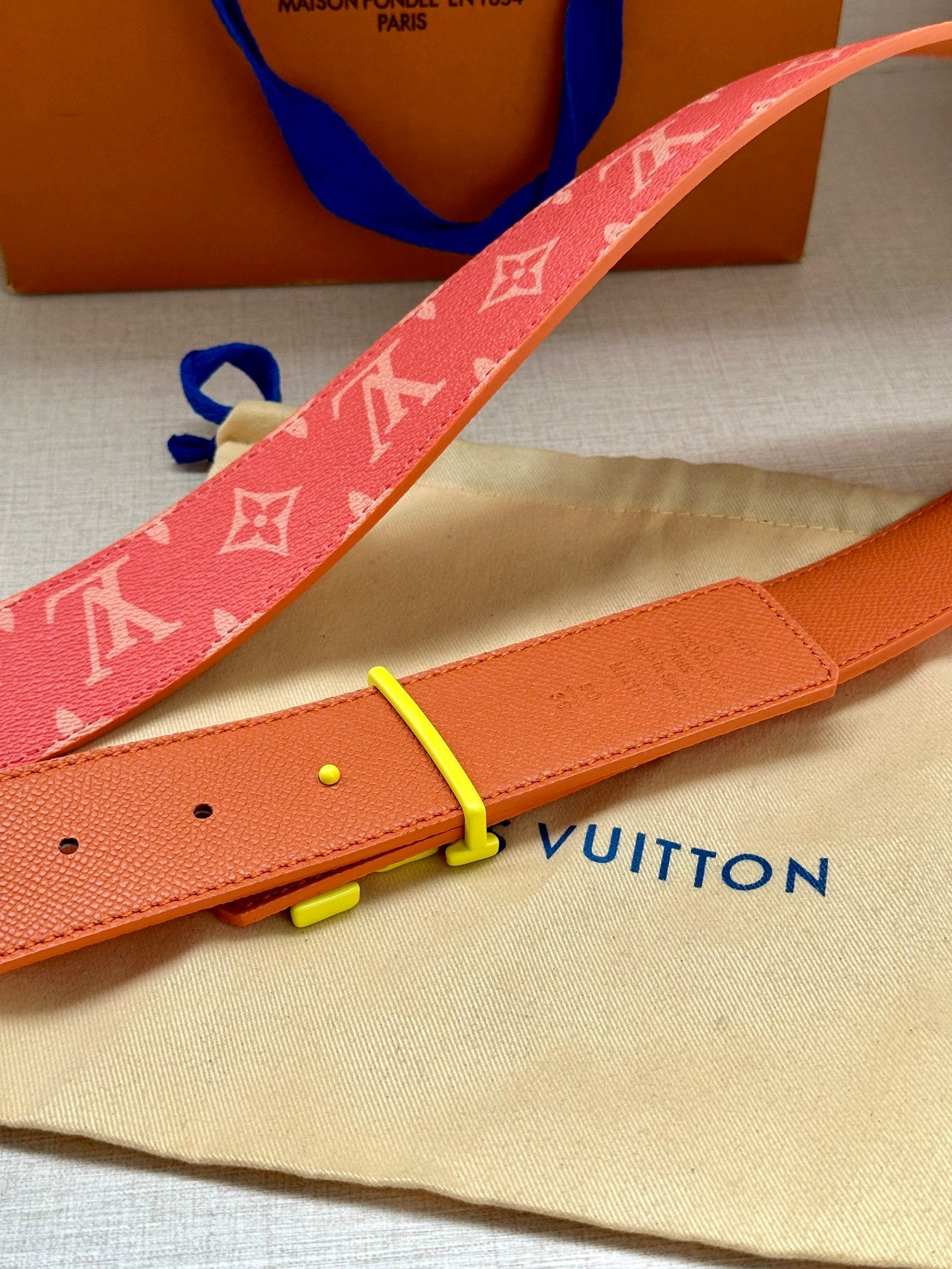 Louis Vuitton belt detail: red monogram strap with gold-tone buckle and orange leather back.