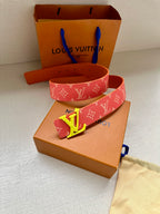 Louis Vuitton belt with red monogram strap and gold-tone LV buckle, next to gift bag.