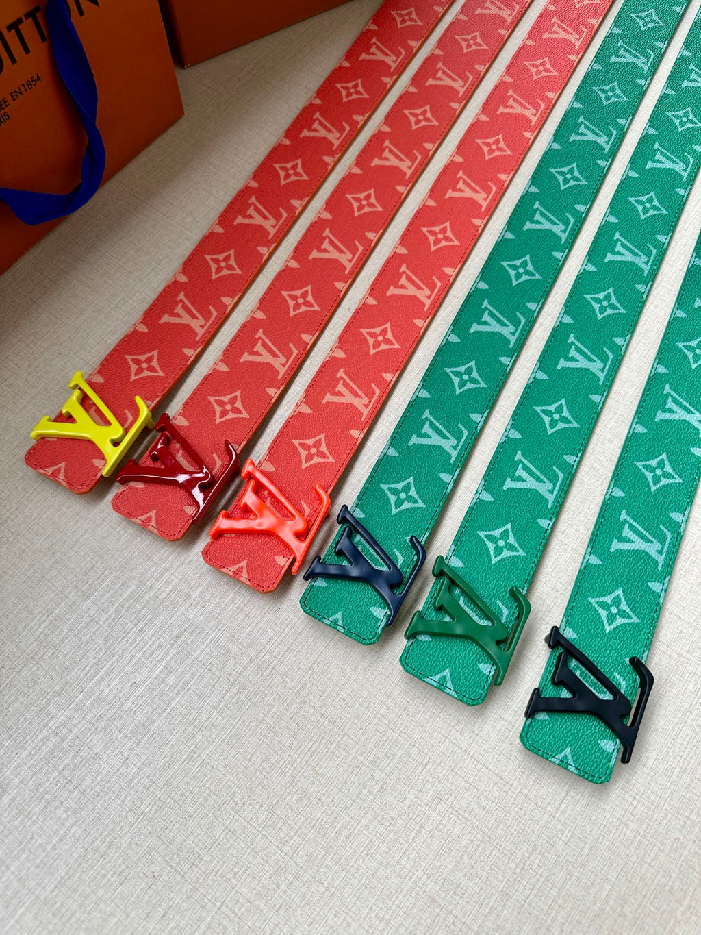 Set of Louis Vuitton belts with monogram straps in red and green tones, with gold buckles.