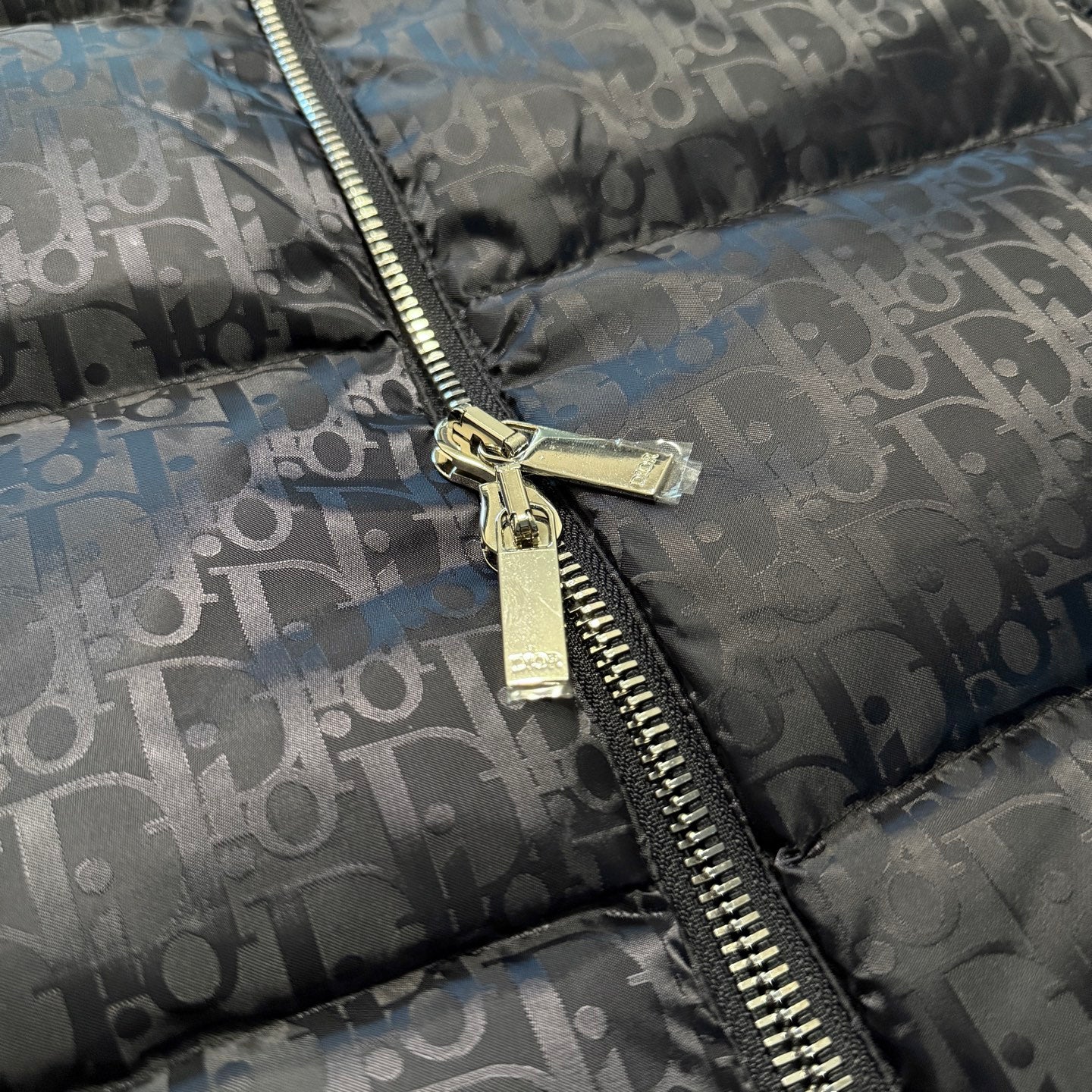 Gold zipper hardware on Dior logo puffer jacket, gray-blue monogram pattern, close-up.