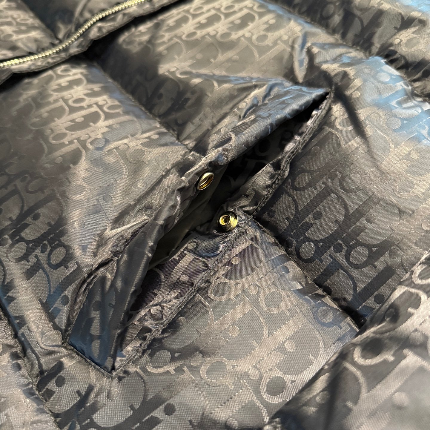 Long puffer jacket with Dior monogram pattern and gold snaps at placket, close-up.