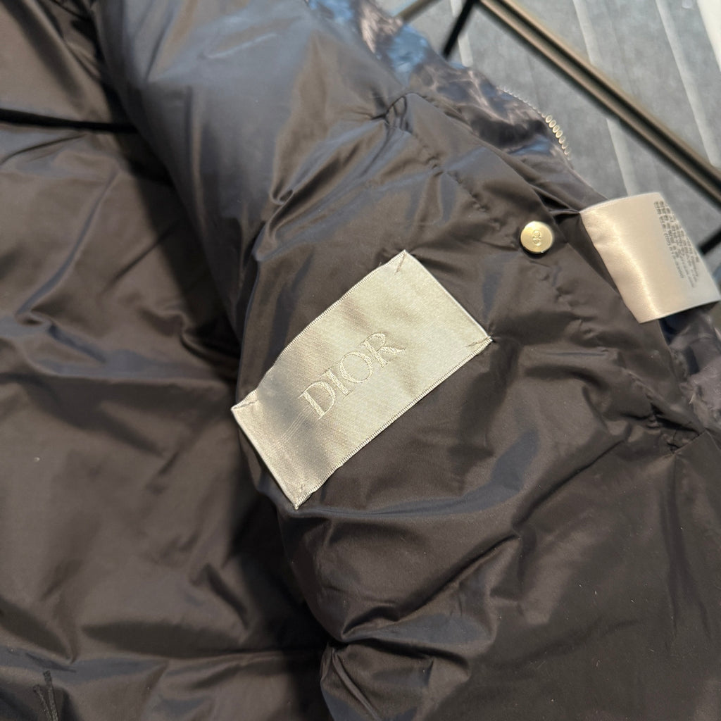 Dior logo fabric label on sleeve cuff of long puffer jacket, dark gray-blue.