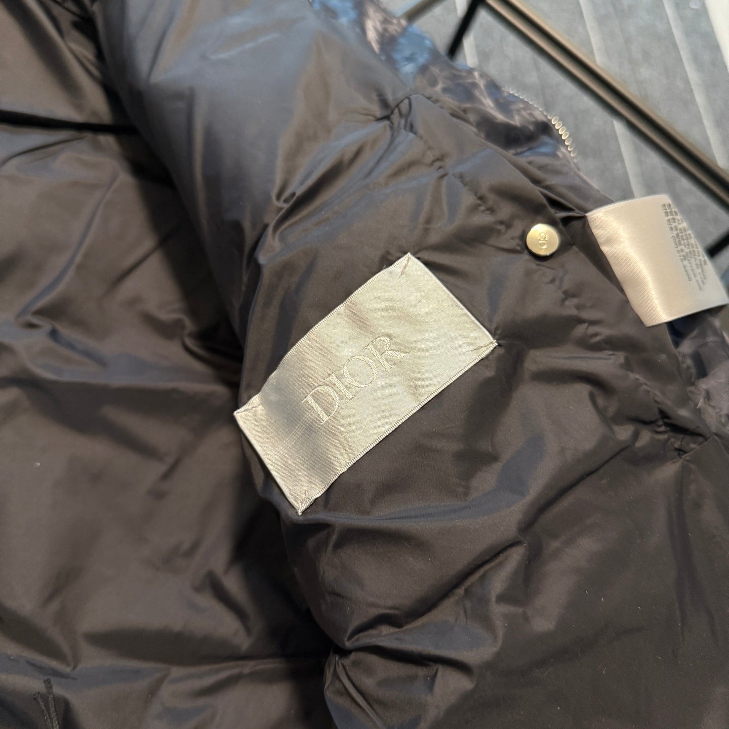 Dior logo fabric label on sleeve cuff of long puffer jacket, dark gray-blue.