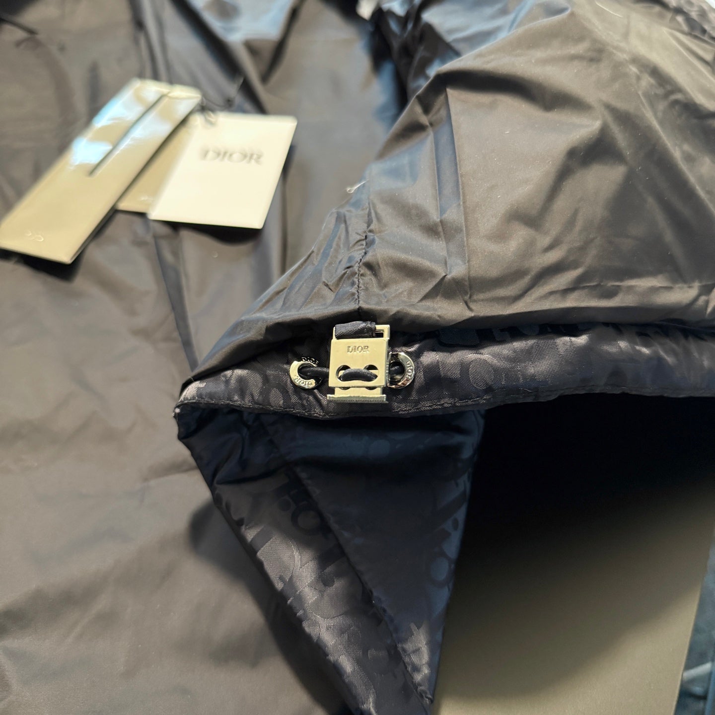 Long puffer jacket hem with Dior snap tab and logo pattern, close-up detail.