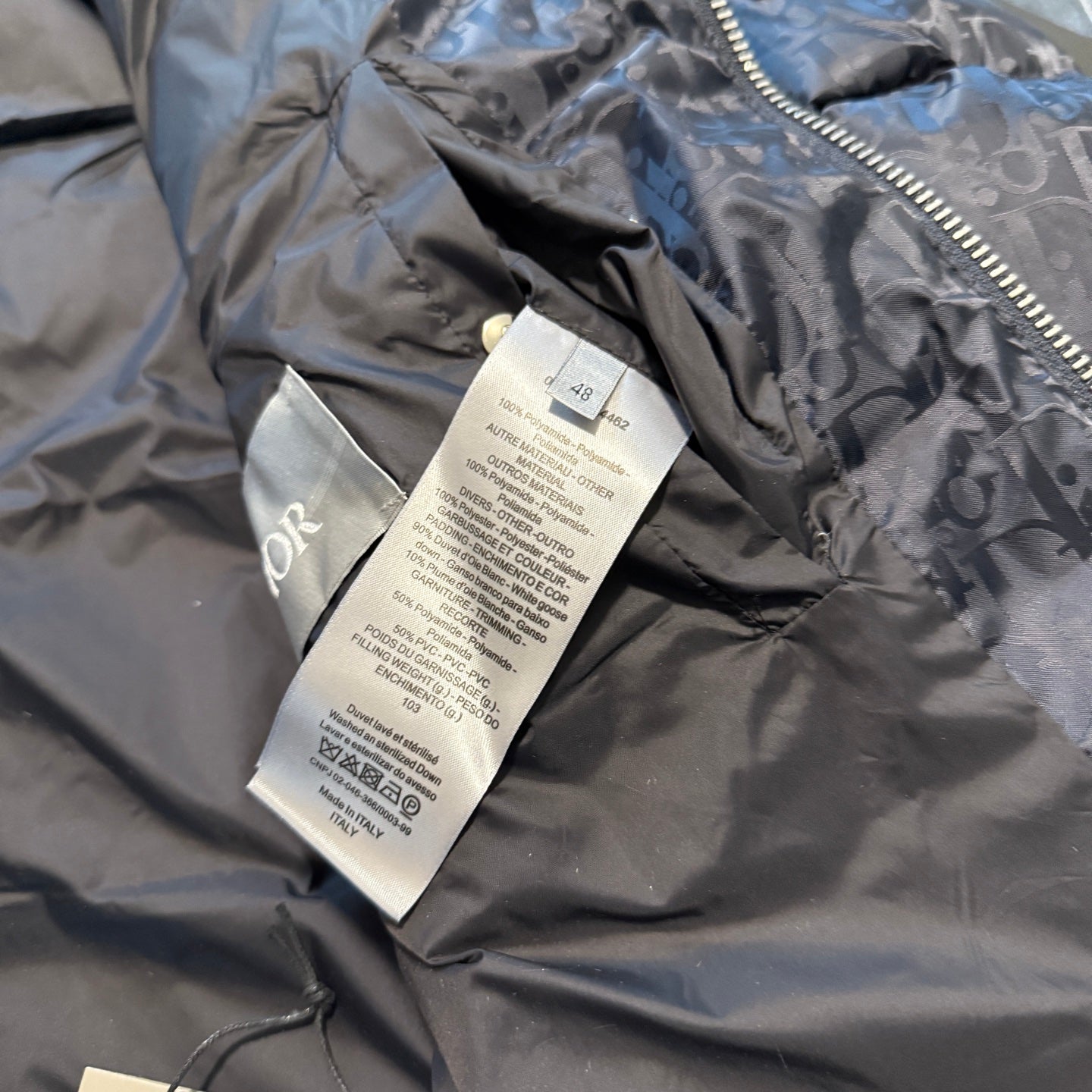 Dior size and care tags on interior lining of dark logo puffer jacket, close-up.