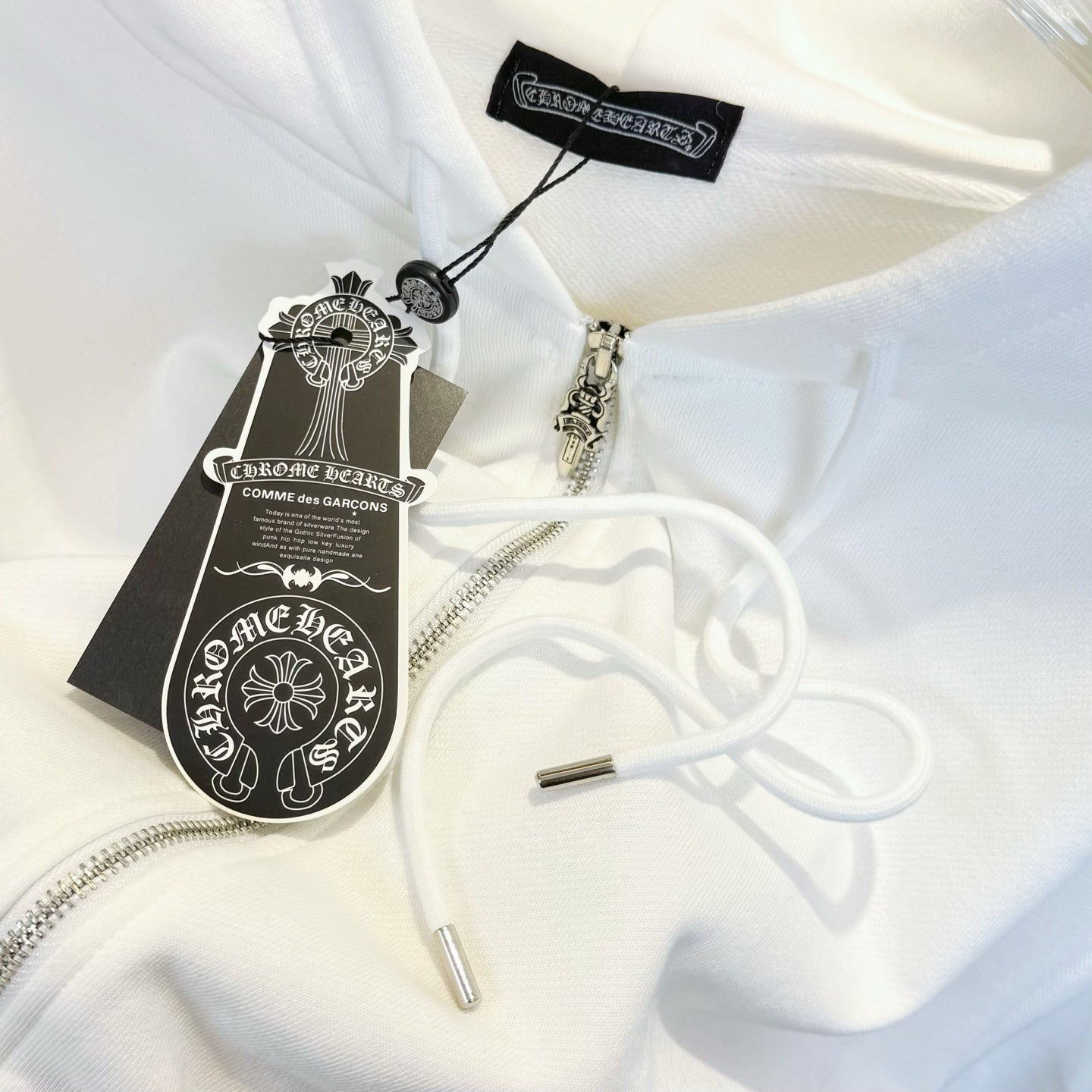 White zip hoodie close-up with drawstrings and hanging brand tags
