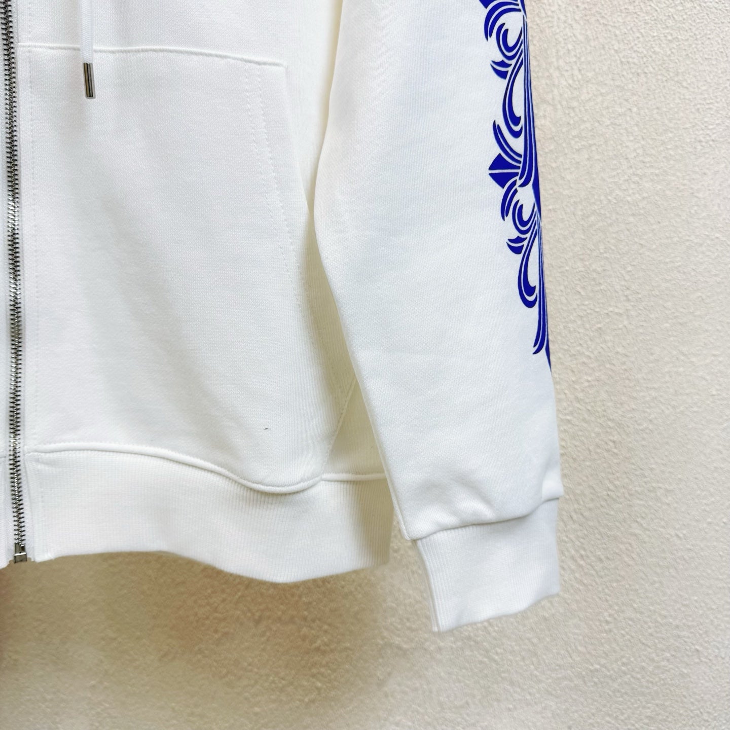 White hoodie pocket area with partial front zipper and blue sleeve graphic