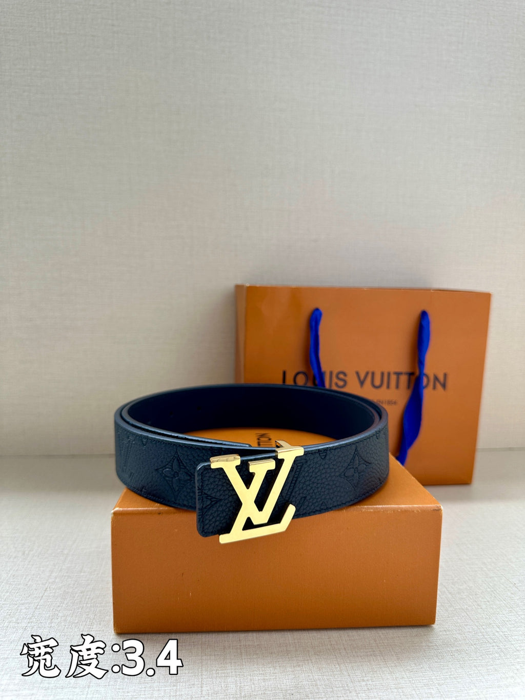 Dark blue leather belt with LV buckle on display next to the box
