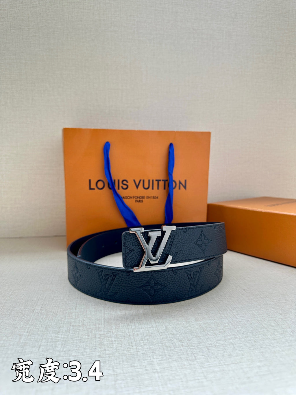 Dark blue leather belt with silver-tone LV buckle, resting on the box