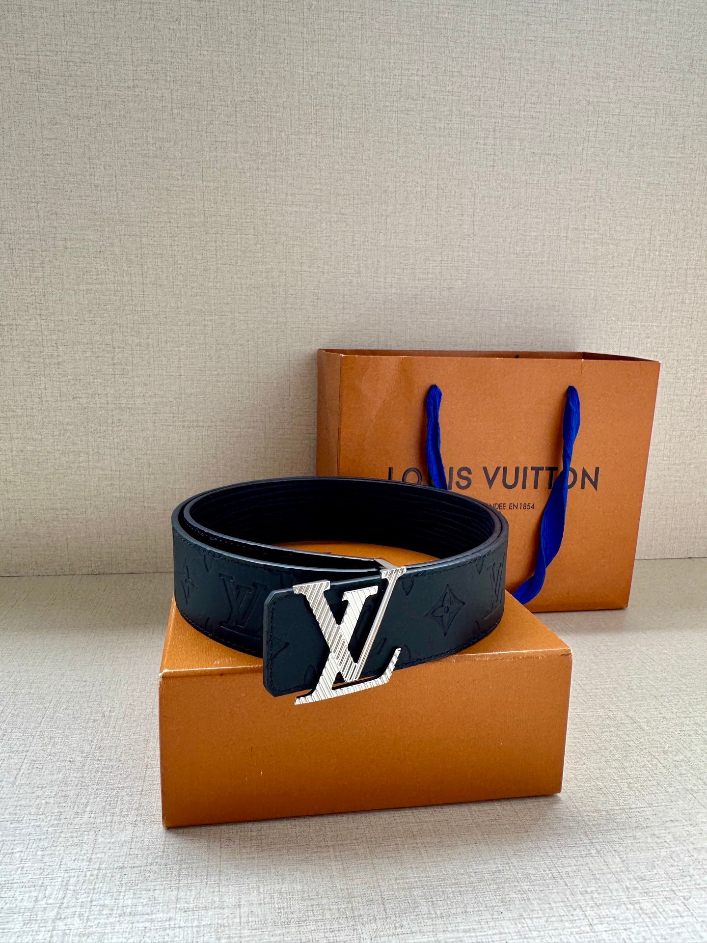 Dark blue leather belt with large gold-toned LV buckle, laid for display