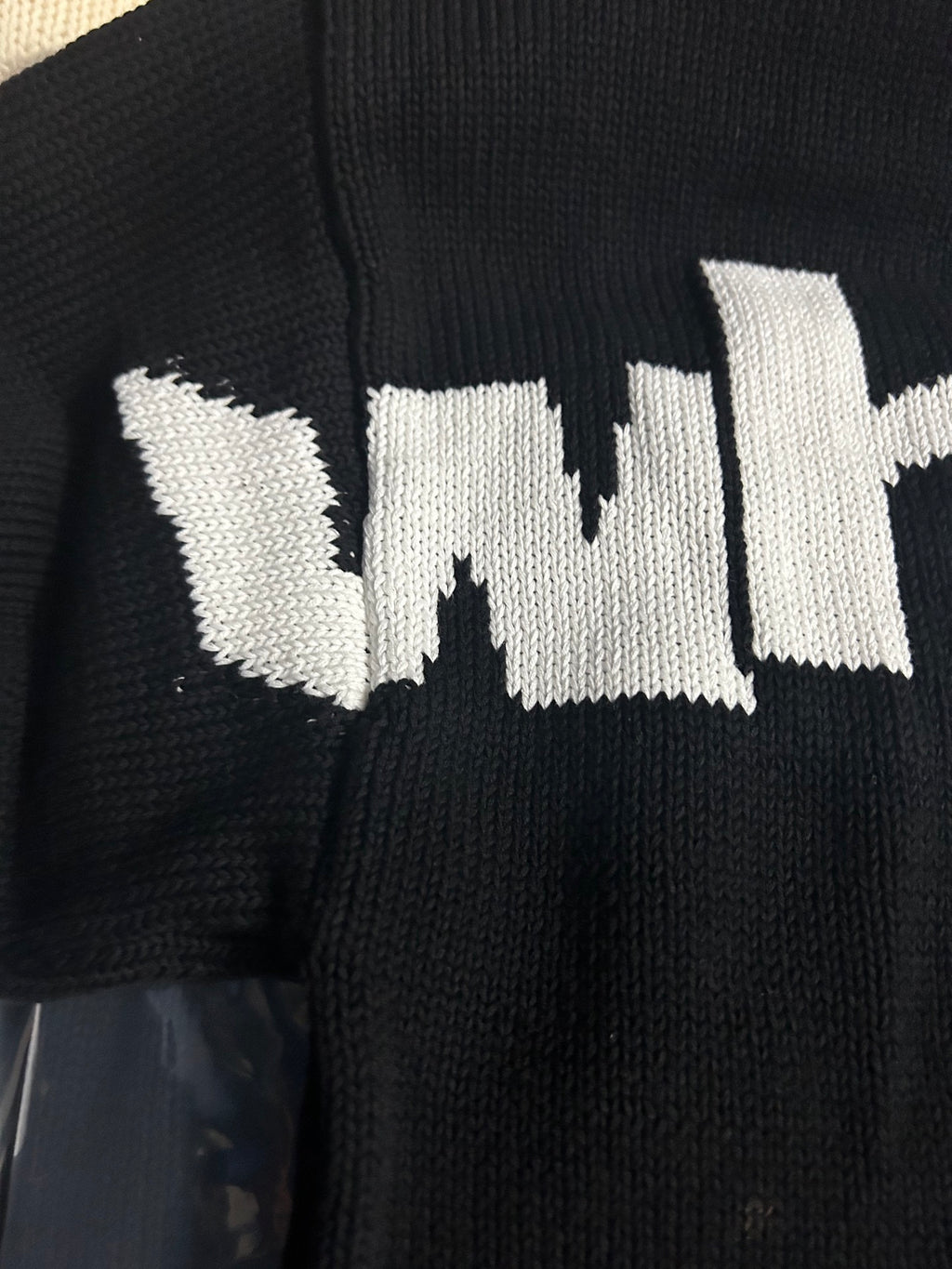 Black knit sweater close-up of white 'wit' text logo