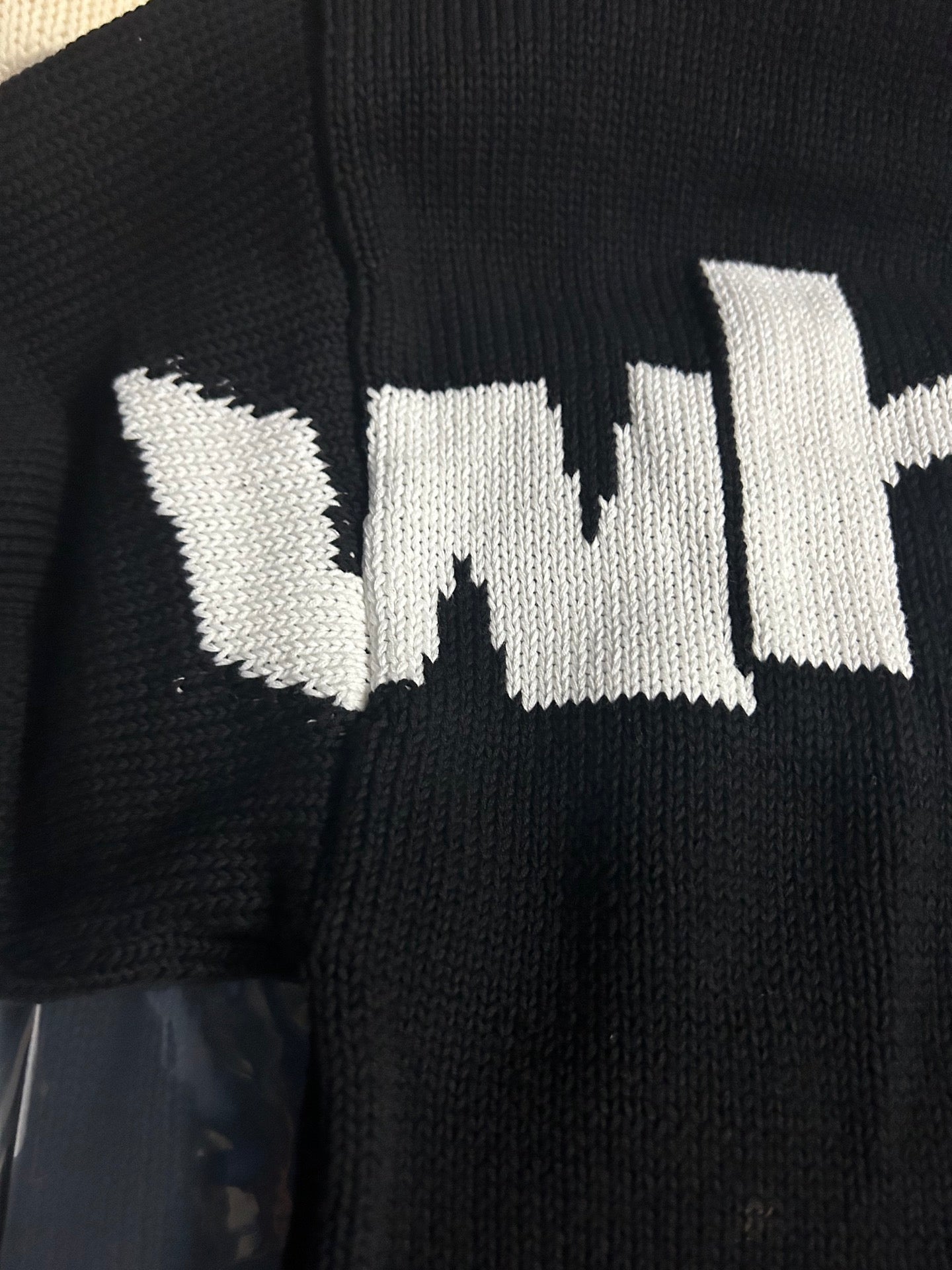 Black knit sweater close-up of white 'wit' text logo