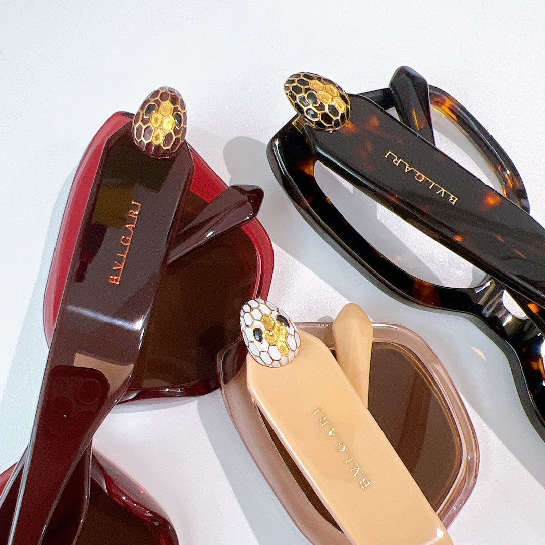 Sunglasses close-up showing red, beige, and dark frames with gold medallion temples