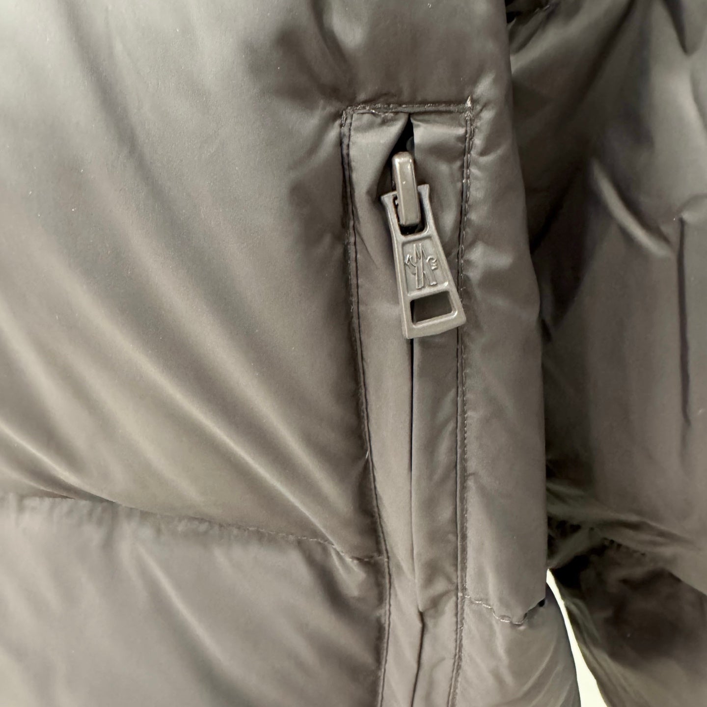 Logo zipper pull on dark puffer jacket lining with stitched panel edges