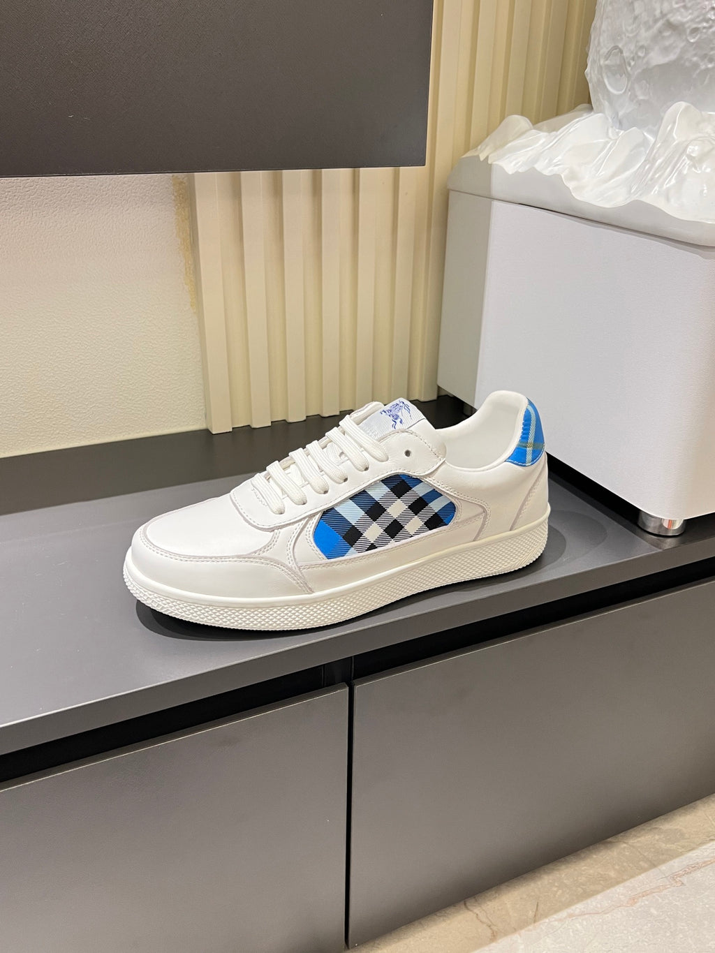 White Burberry low-top sneakers on display, blue and black check front panel