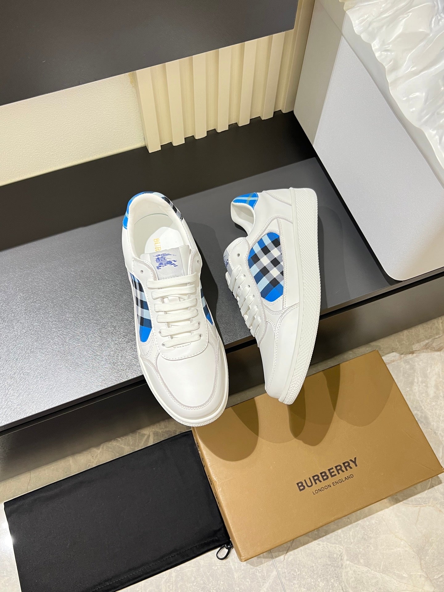 White Burberry sneaker pair on box, white uppers with blue check accents