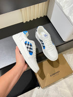 White Burberry sneakers held in hand, blue and black check stripe accents