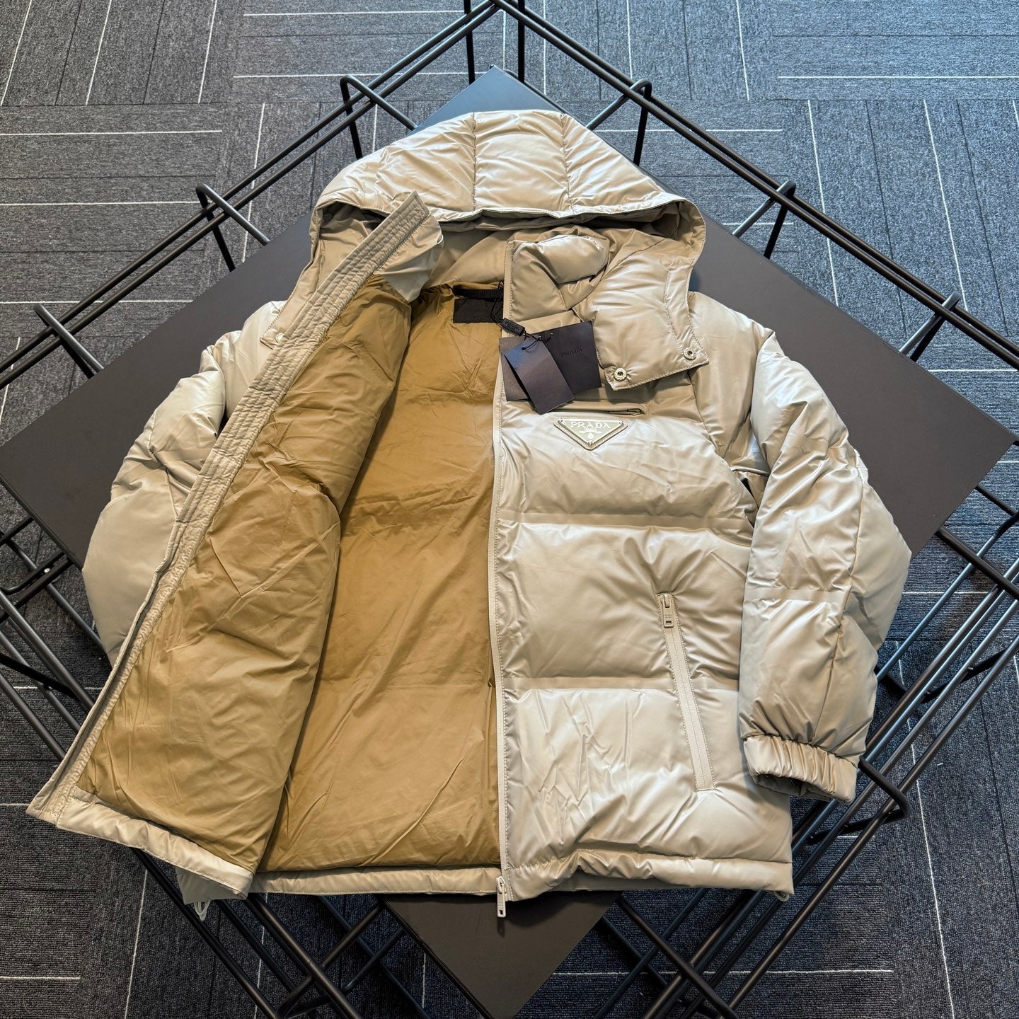 Beige hooded puffer jacket, front zip open showing inner lining and logo patch