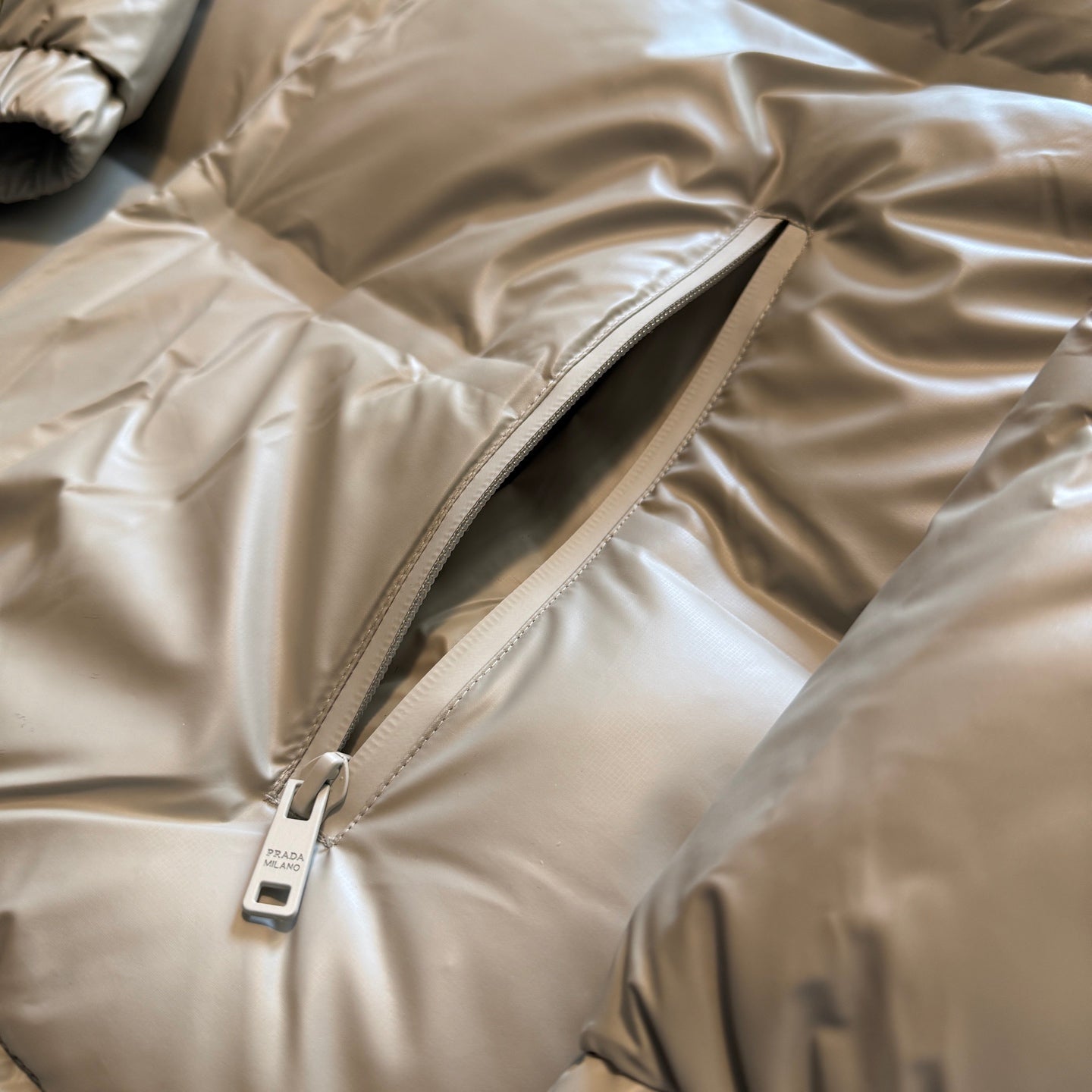 Beige puffer jacket zipper track with logo pull and side seam panel
