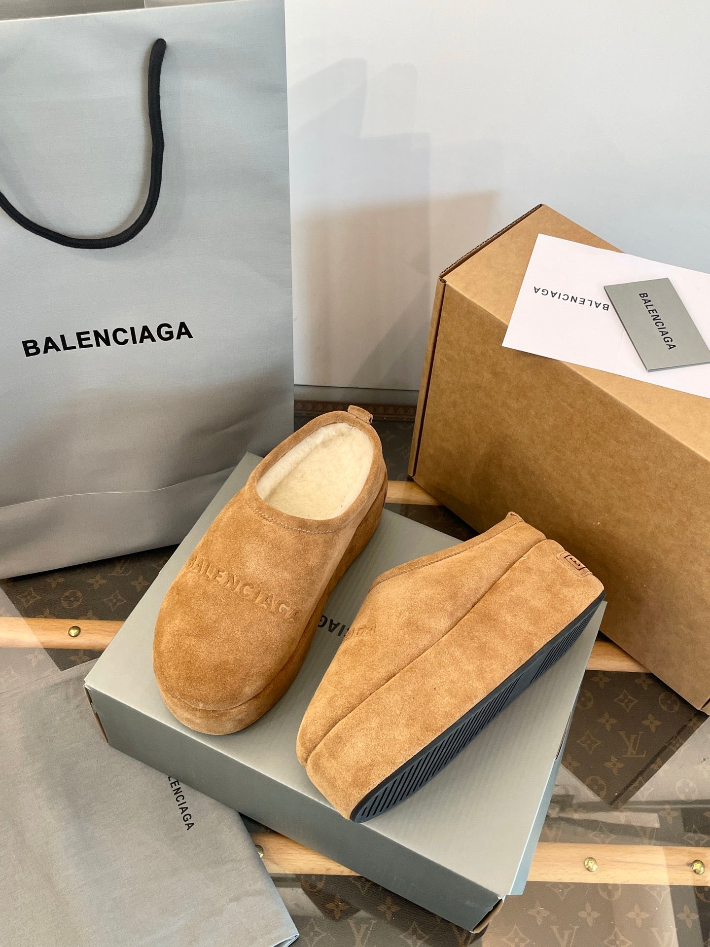 Tan suede slip-on sandals with beige lining, angled view beside a gray shoebox.