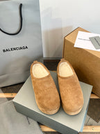 Tan suede slip-on sandals with beige lining and curved toe, shown in a shoe box.