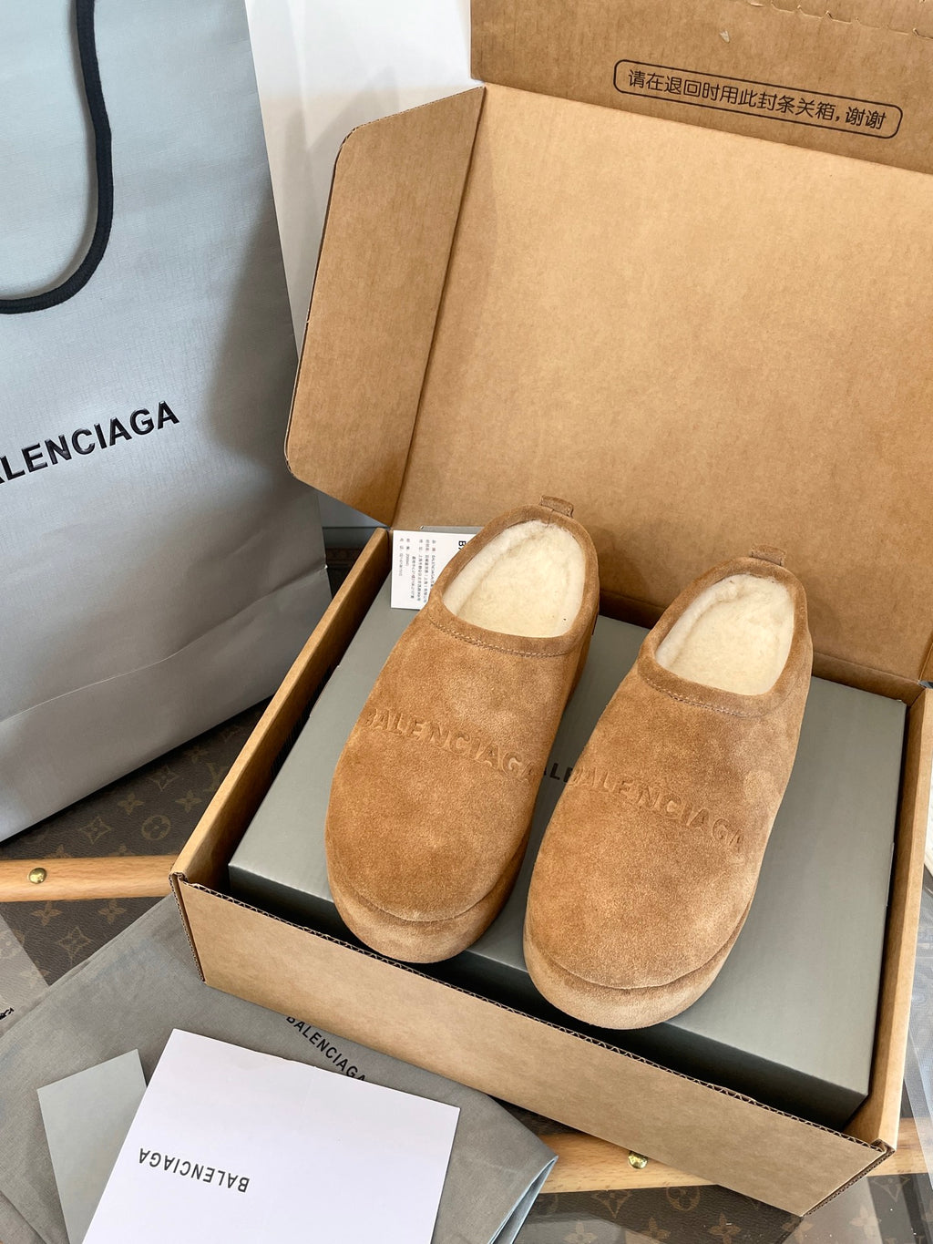 Tan suede slip-on sandals with beige lining, displayed in a shoebox with receipt tag.
